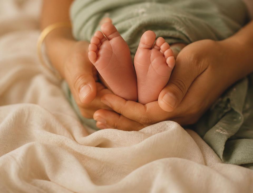 A caregiver's hands cradling a newborn baby's feet on a cream blanket