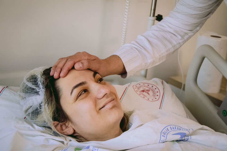 A mother resting in a recovery bed while a caregiver checks on her